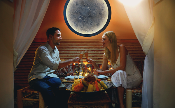 Couple having a romantic dinner with a super moon decorative light on the wall.
